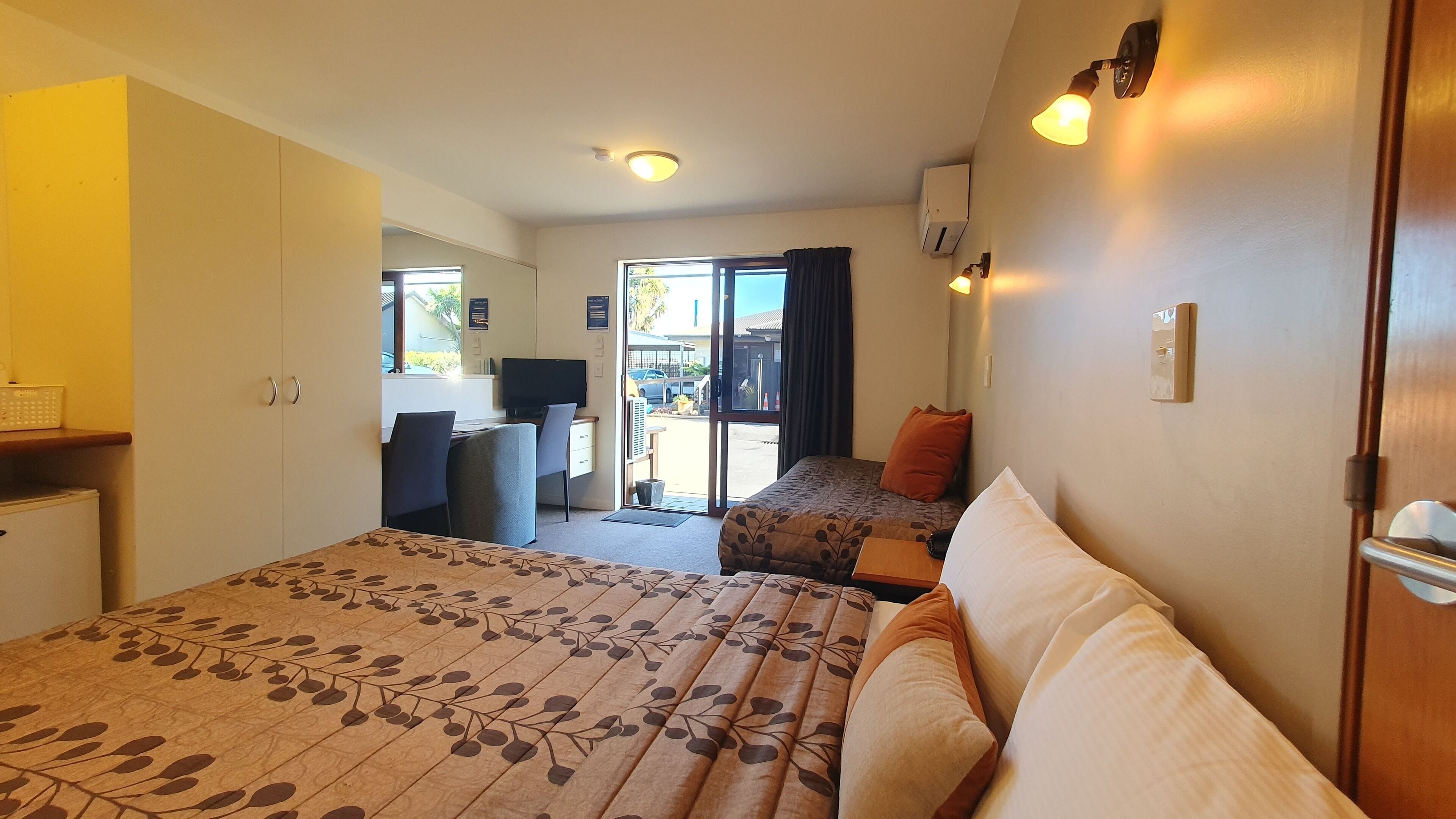 A hotel room with two beds, a desk, and a chair. There is a window with a view of the outside.
