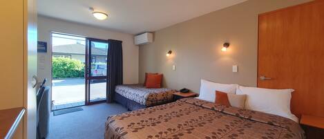 A hotel room with a large bed, a smaller bed, a desk, and a sliding glass door leading to a parking area.
