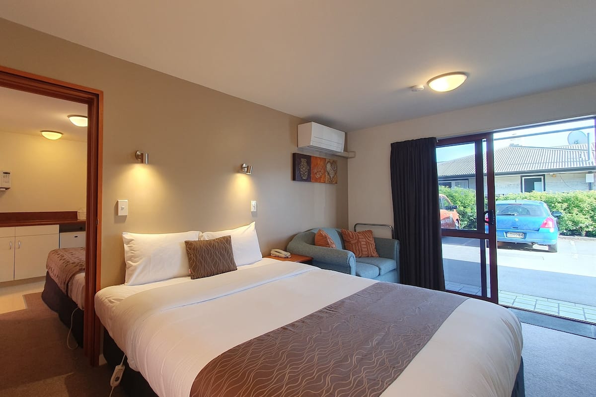 A hotel room with a large bed, a sofa, a small table, a microwave, and a view of the street.