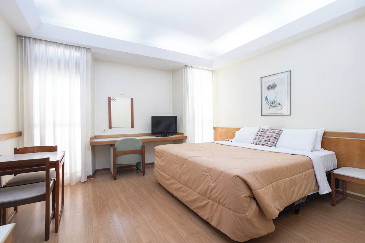 Ein Hotelzimmer mit Bett, Schreibtisch, Stuhl und Fernseher.