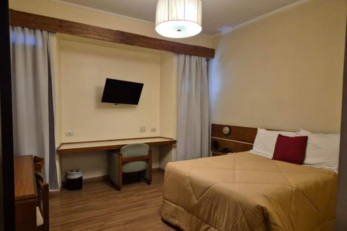 Ein Hotelzimmer mit Bett, Schreibtisch, Stuhl, Fernseher und Lampe.
