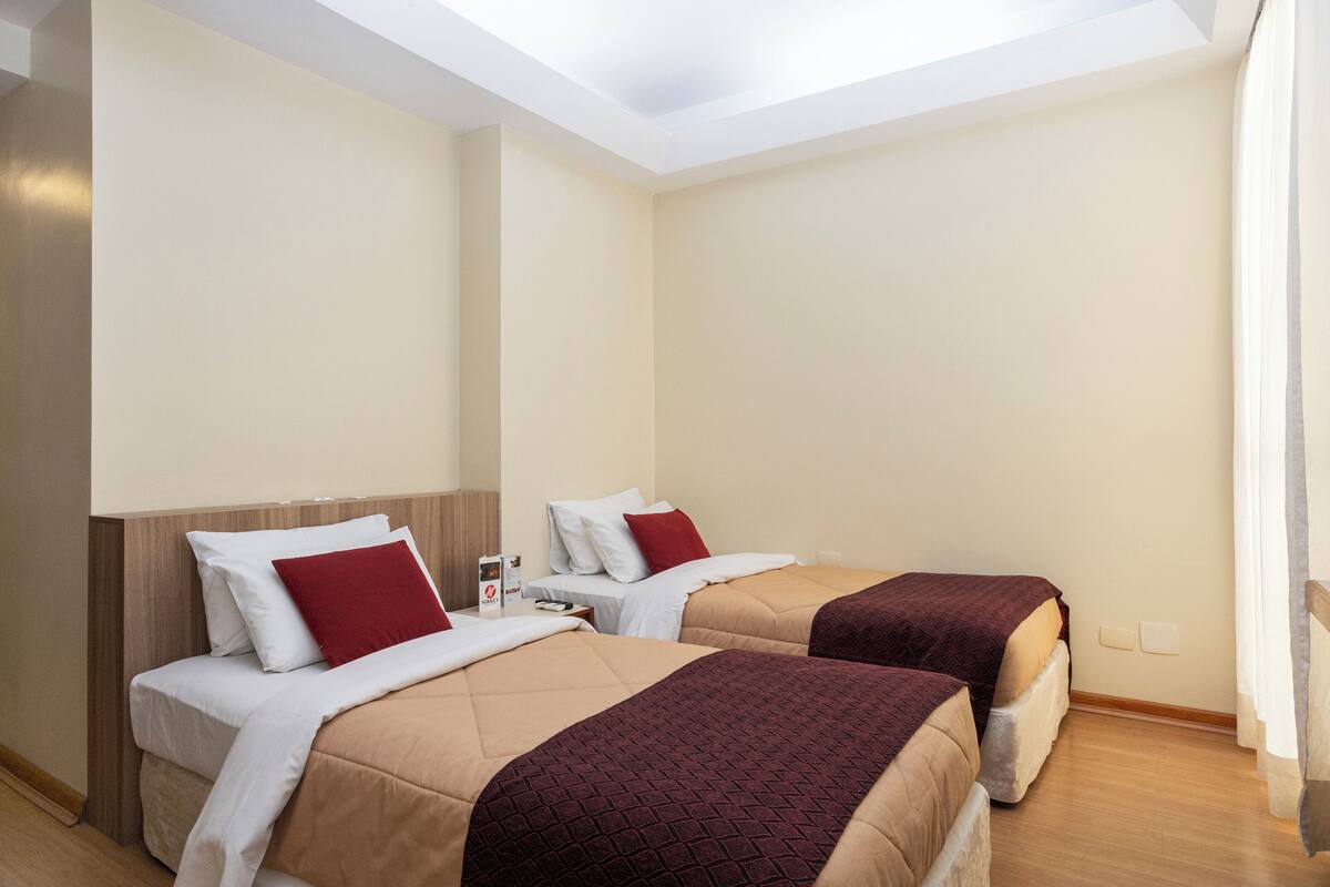 Ein Hotelzimmer mit zwei Betten, jedes mit einem roten und weißen Kopfkissen, und einem hölzernen Kopfteil.