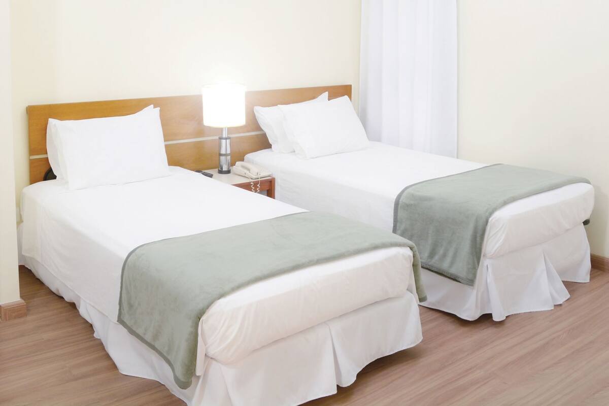 Two single beds with white bedding and green throw blankets, a bedside table with a lamp, and a telephone.