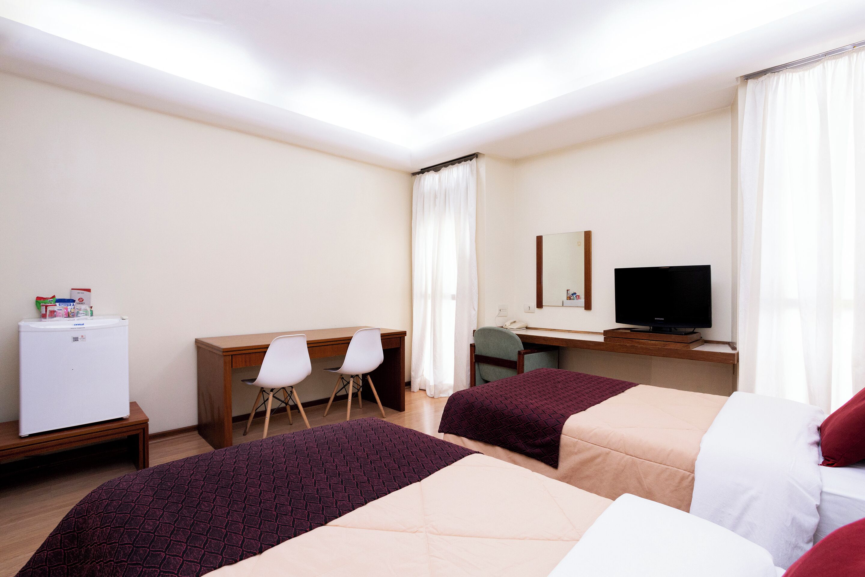 Habitación de hotel con dos camas, un escritorio, una silla, un televisor y un refrigerador.