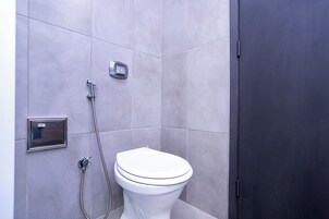 Moderni kylpyhuone, jossa on wc, suihku ja seinälle asennettu ohjauspaneeli.