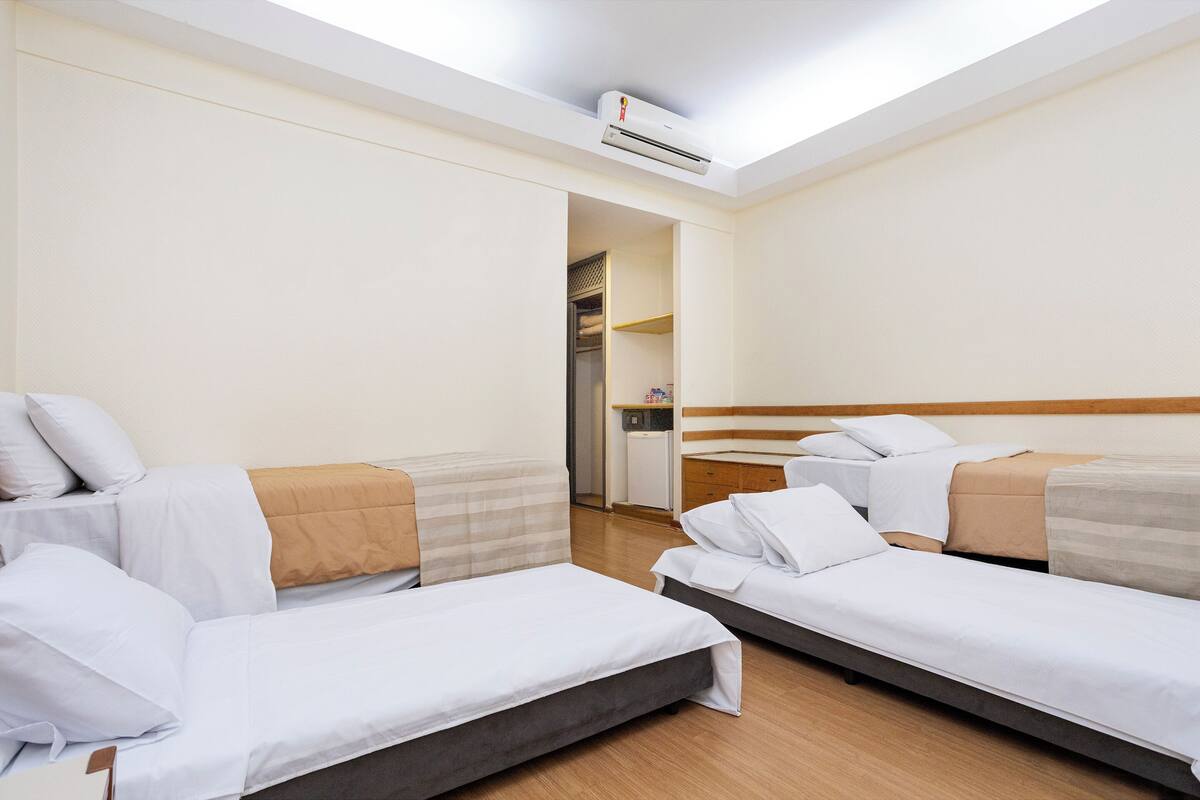 Ein Hotelzimmer mit zwei Einzelbetten, Holzboden, einem Kleiderschrank und einer kleinen Küchenzeile.
