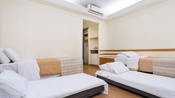A hotel room with two single beds, a wooden floor, a wardrobe, and a small kitchenette.