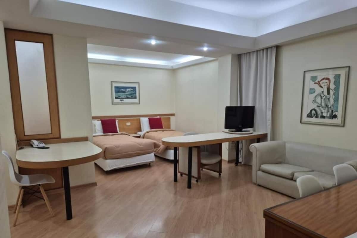 Ein Hotelzimmer mit Bett, Schreibtisch, Fernseher, Sofa und einem Bild an der Wand.
