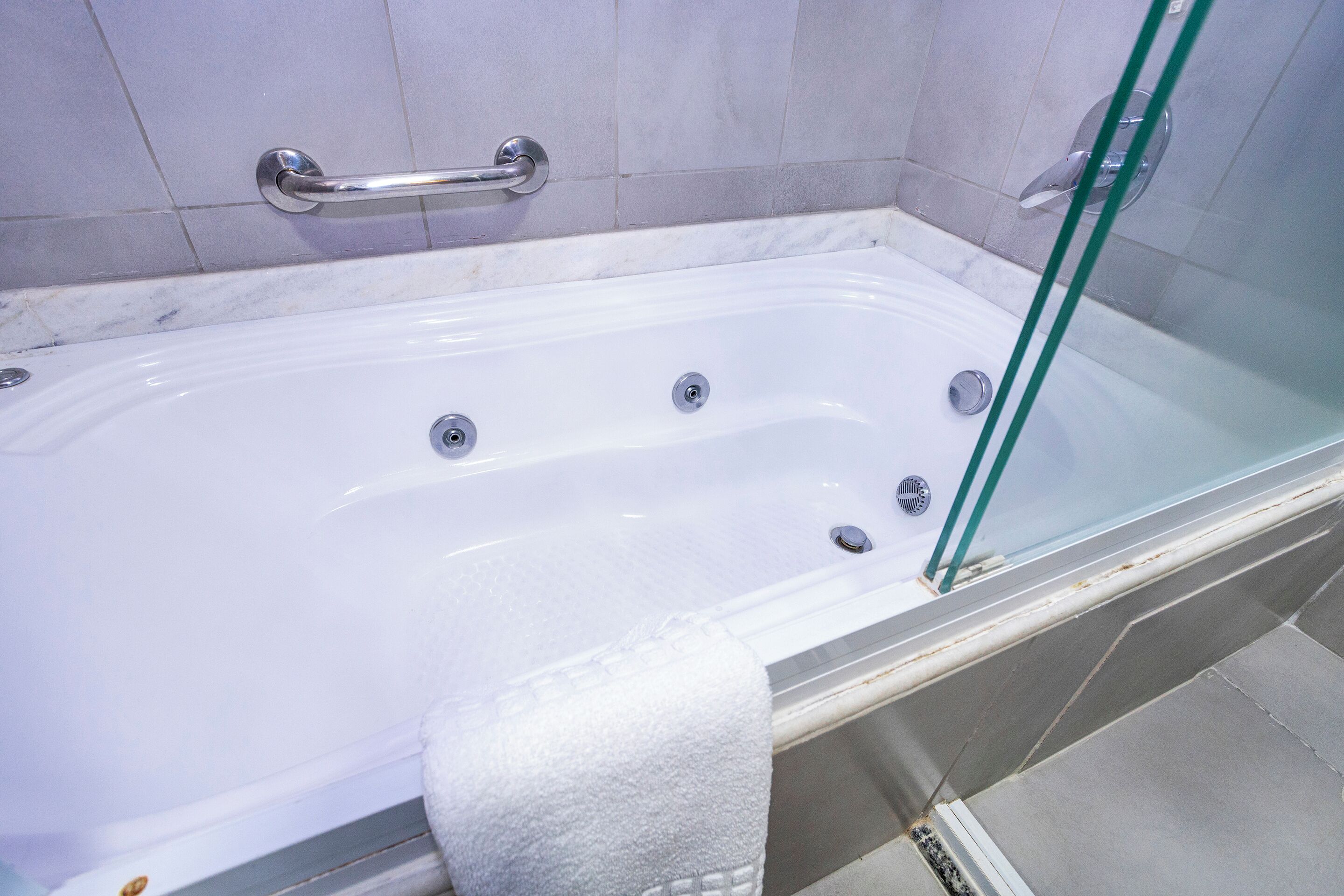 A bathtub with a glass enclosure, a metal grab bar, and a white towel.