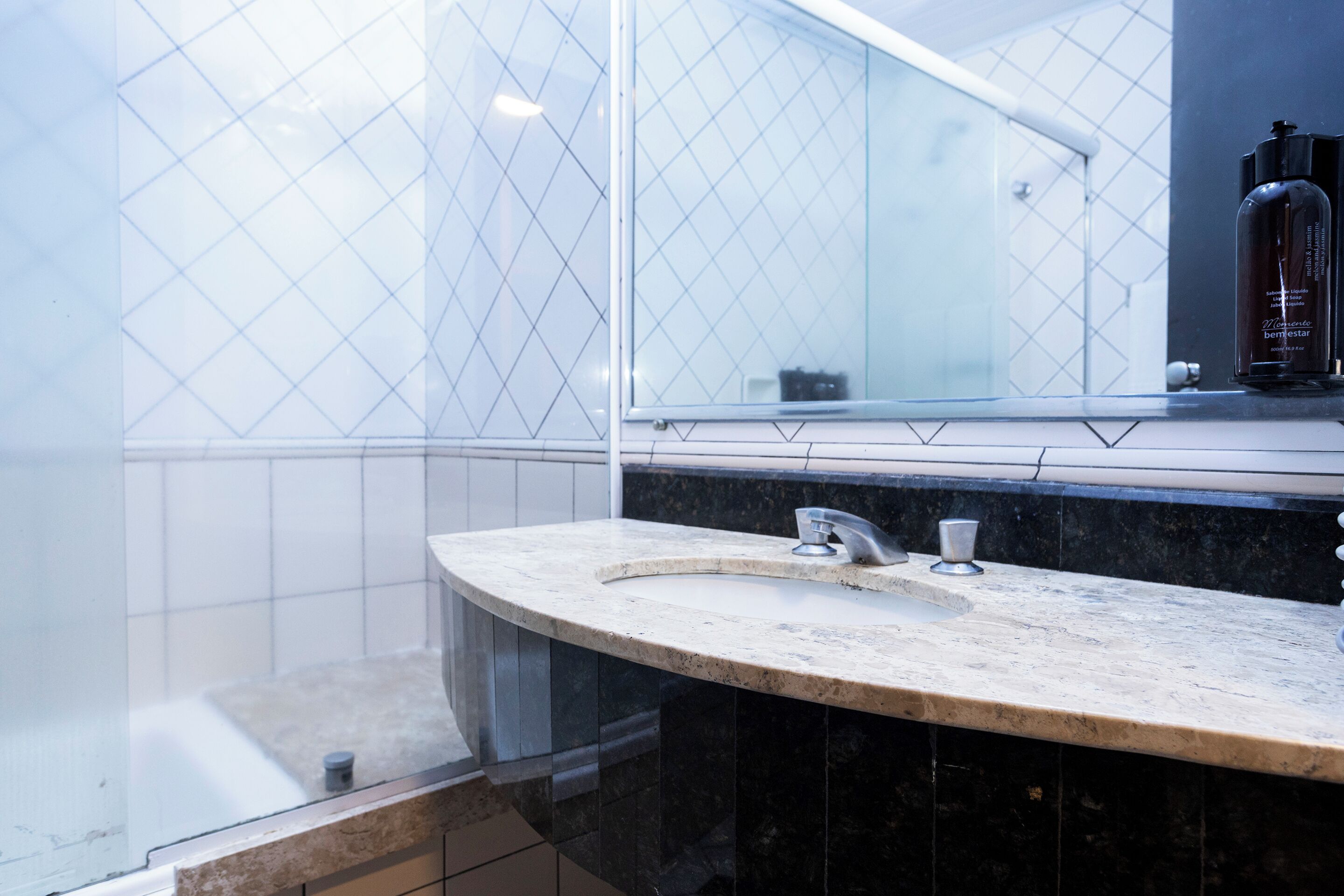 Ein Badezimmer mit einem gewölbten Marmorwaschbecken, einem Spiegel und einer Duschkabine aus Glas.