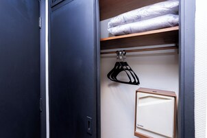 A closet with a hanging rack, a shelf with folded linens, and a framed item on the wall.
