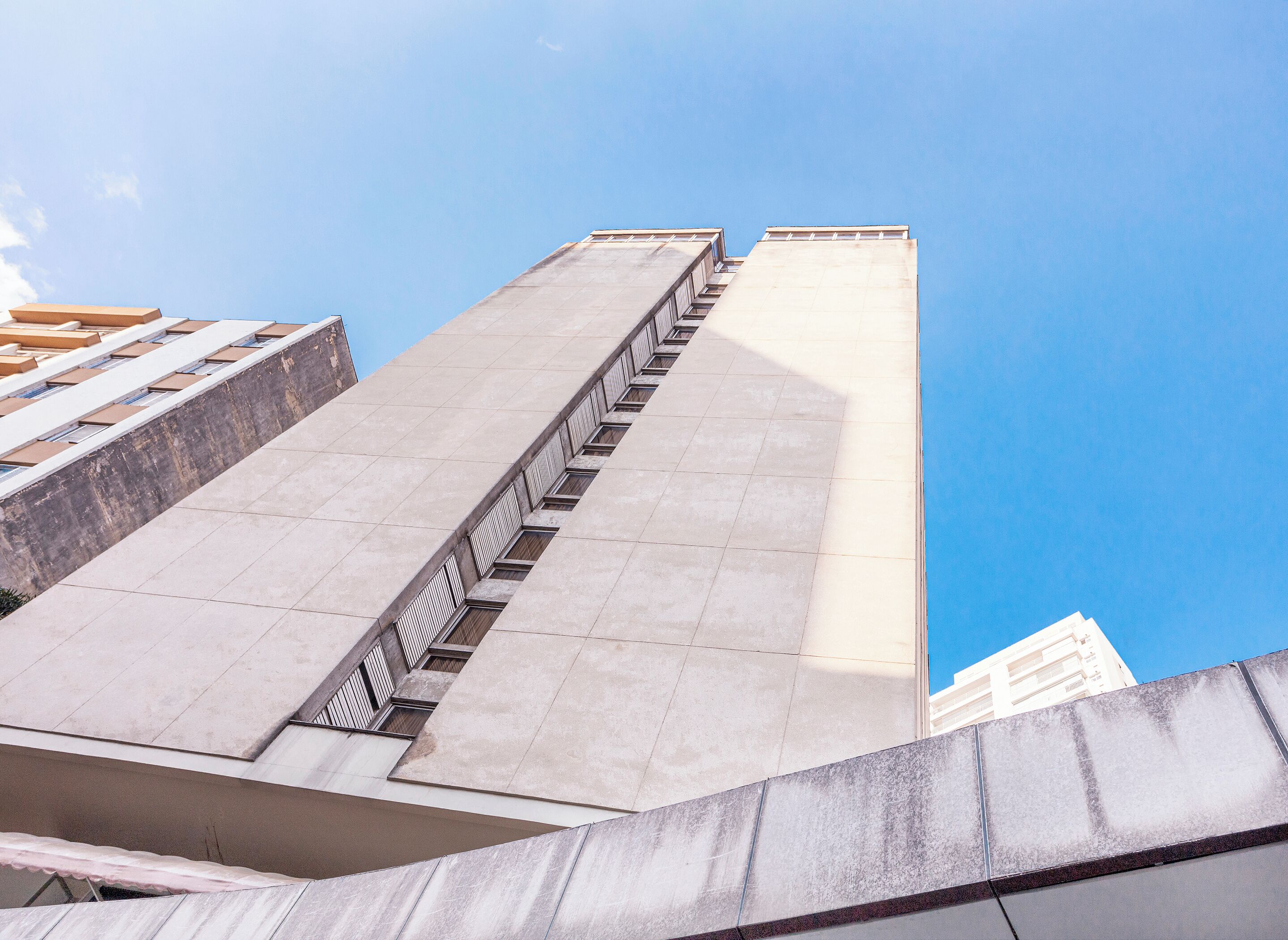 A high-rise building with a modern architectural design, featuring a prominent staircase and a clear blue sky in the background.