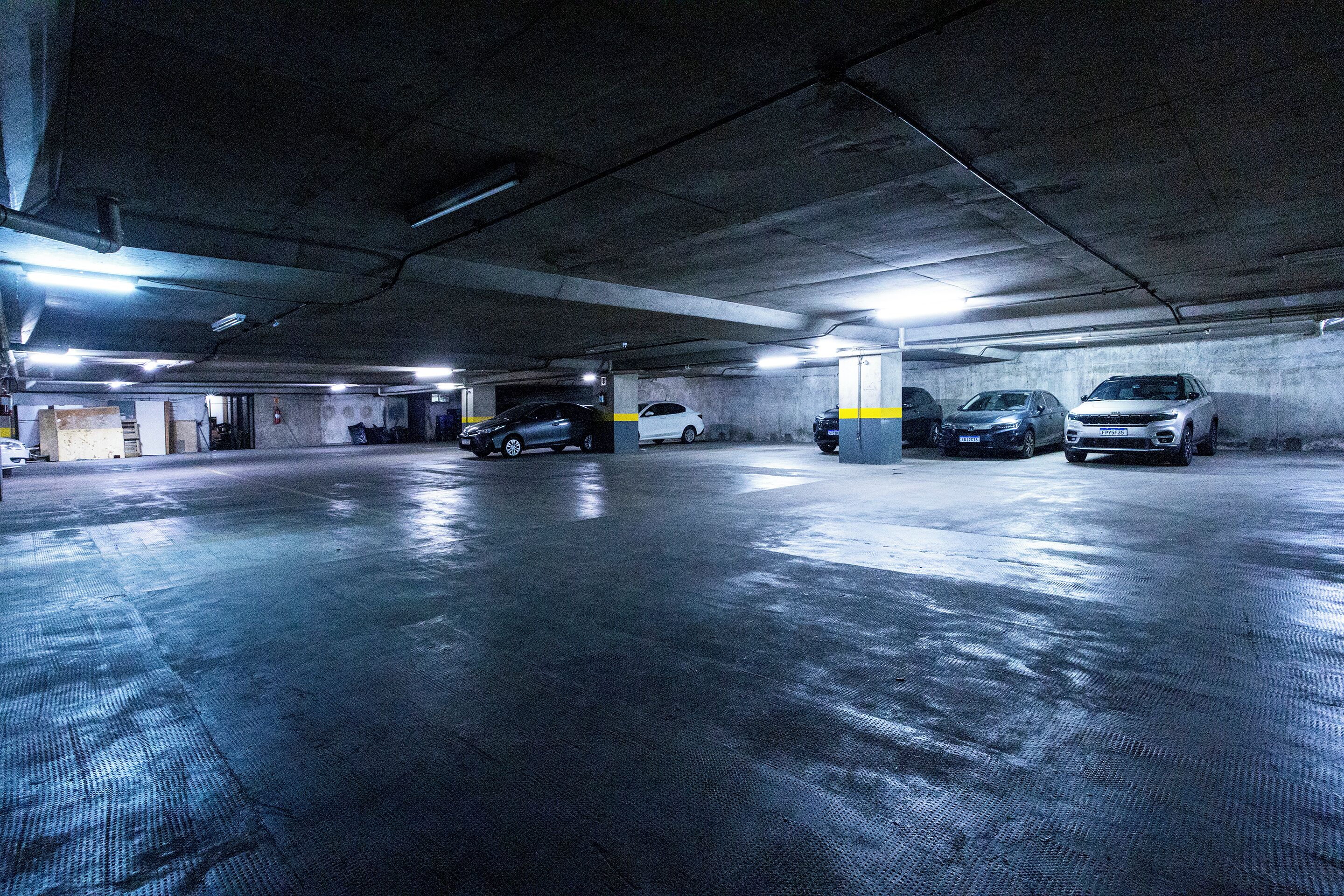 Un garaje subterráneo con pisos y paredes de hormigón, que muestra varios coches estacionados e iluminación en el techo.