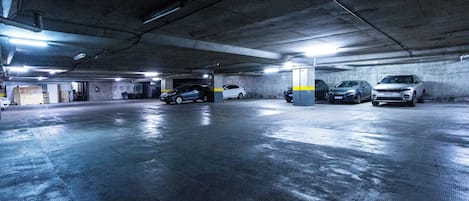 Un garaje subterráneo con pisos y paredes de hormigón, que muestra varios coches estacionados e iluminación en el techo.
