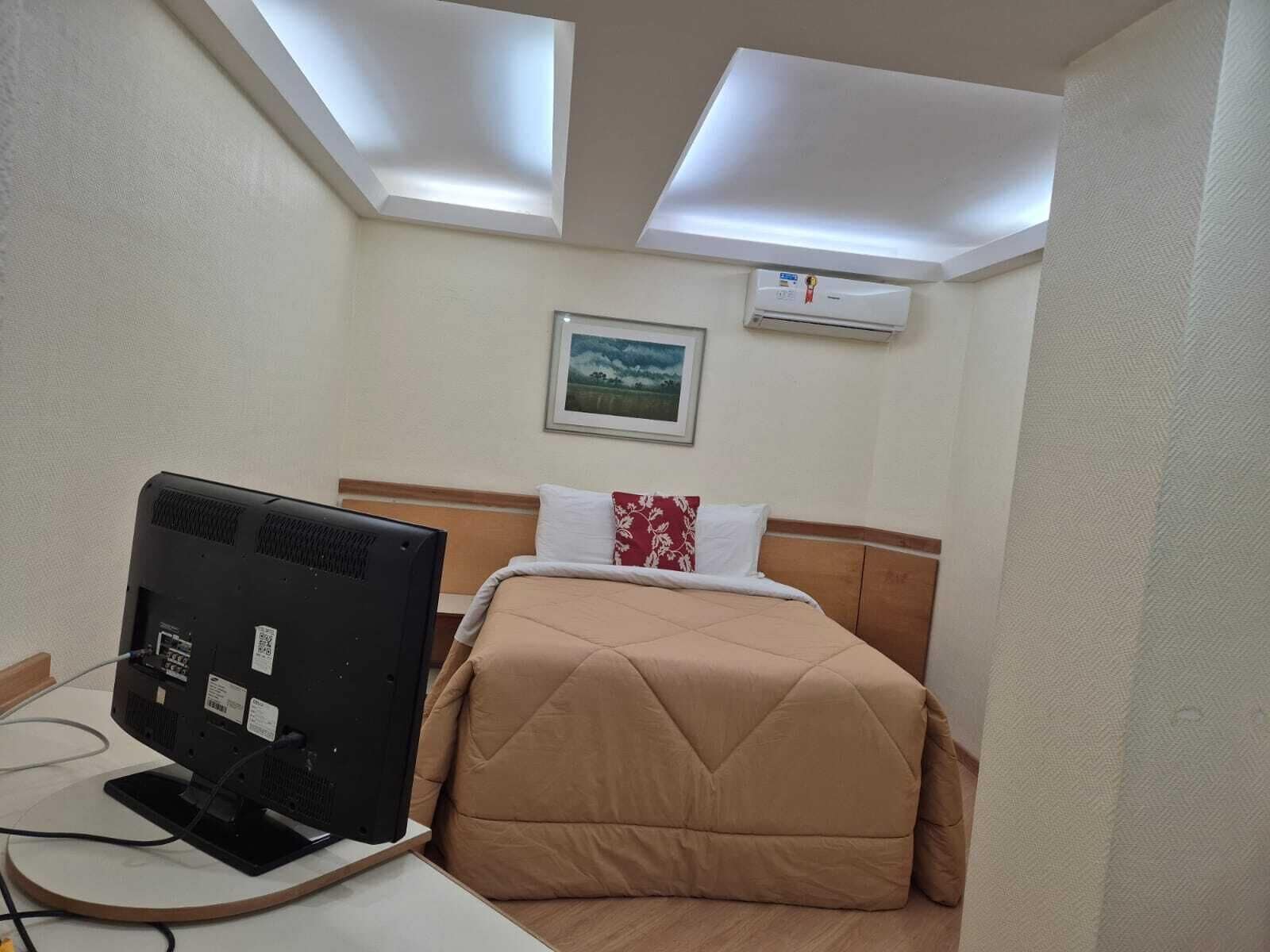 Una habitación de hotel con una cama, un escritorio con computadora, aire acondicionado y un cuadro en la pared.