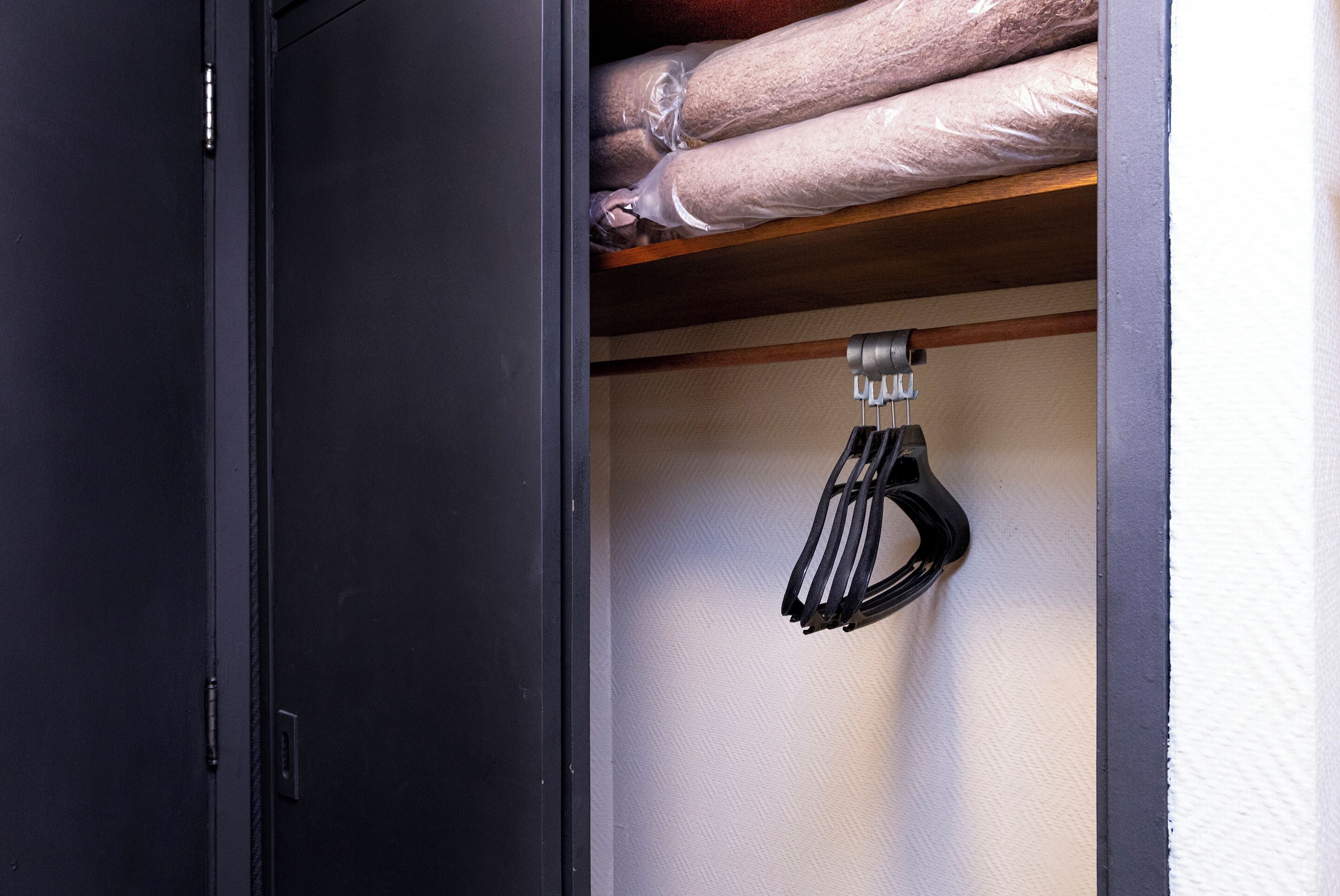 A storage area with a black cabinet and a shelf with rolled-up items and a black object hanging on the wall.