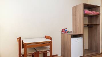 Una habitación compacta con una mesa y sillas de madera, un refrigerador blanco pequeño y un armario de madera con un cojín rosa.