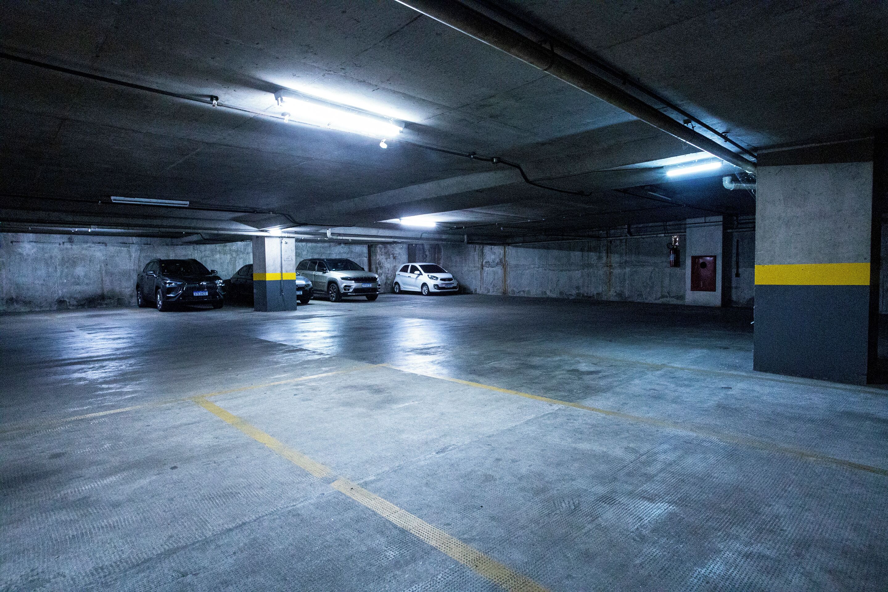 Un parking souterrain à plusieurs niveaux, avec des murs en béton et des lignes jaunes délimitant les places de stationnement.