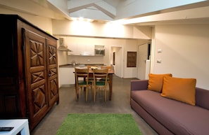 A compact living space with a dining area, kitchenette, and a sofa with orange cushions.