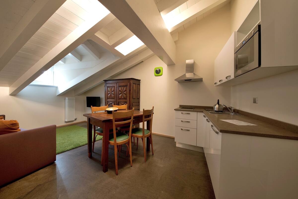 A compact kitchen with a dining area, a radiator, and a clock on the wall.