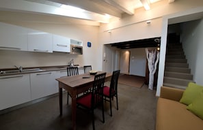 Eine kleine Küche mit weißen Schränken, einem Holztisch mit roten Stühlen, einer Treppe zu einer anderen Ebene und einem Sofa mit grünen Kissen.