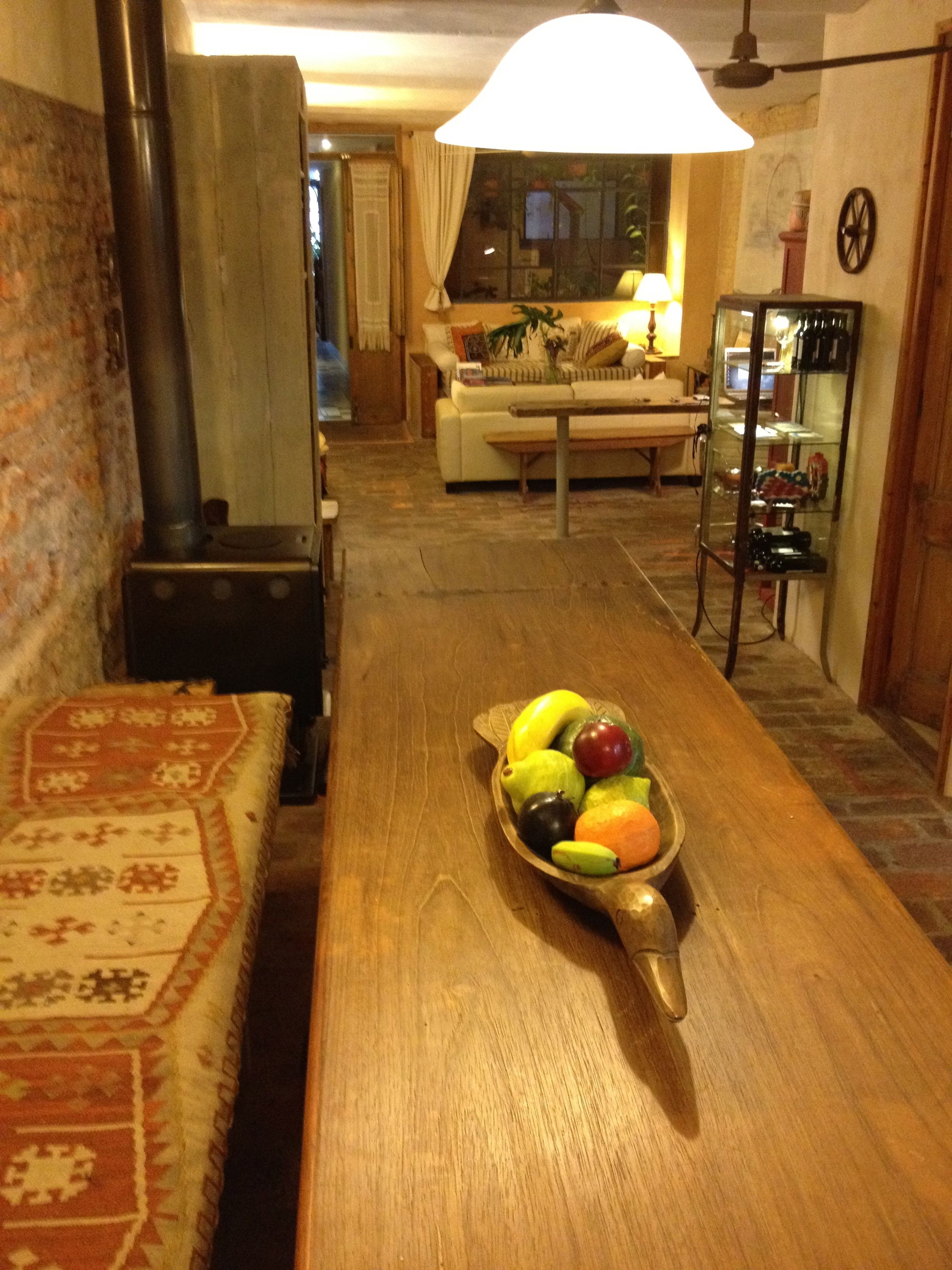 A cozy living room with a wooden coffee table holding a fruit bowl, a sofa, a fireplace, and a dining area in the background.