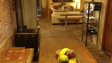 A cozy living room with a wooden coffee table holding a fruit bowl, a sofa, a fireplace, and a dining area in the background.