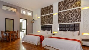 Une chambre d’hôtel avec deux lits, un plancher en bois, un coin repas avec des chaises et un papier peint à motifs.