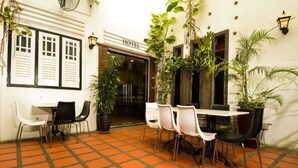 Une cour d’hôtel avec un sol carrelé, des chaises blanches et noires, et des plantes en pot.