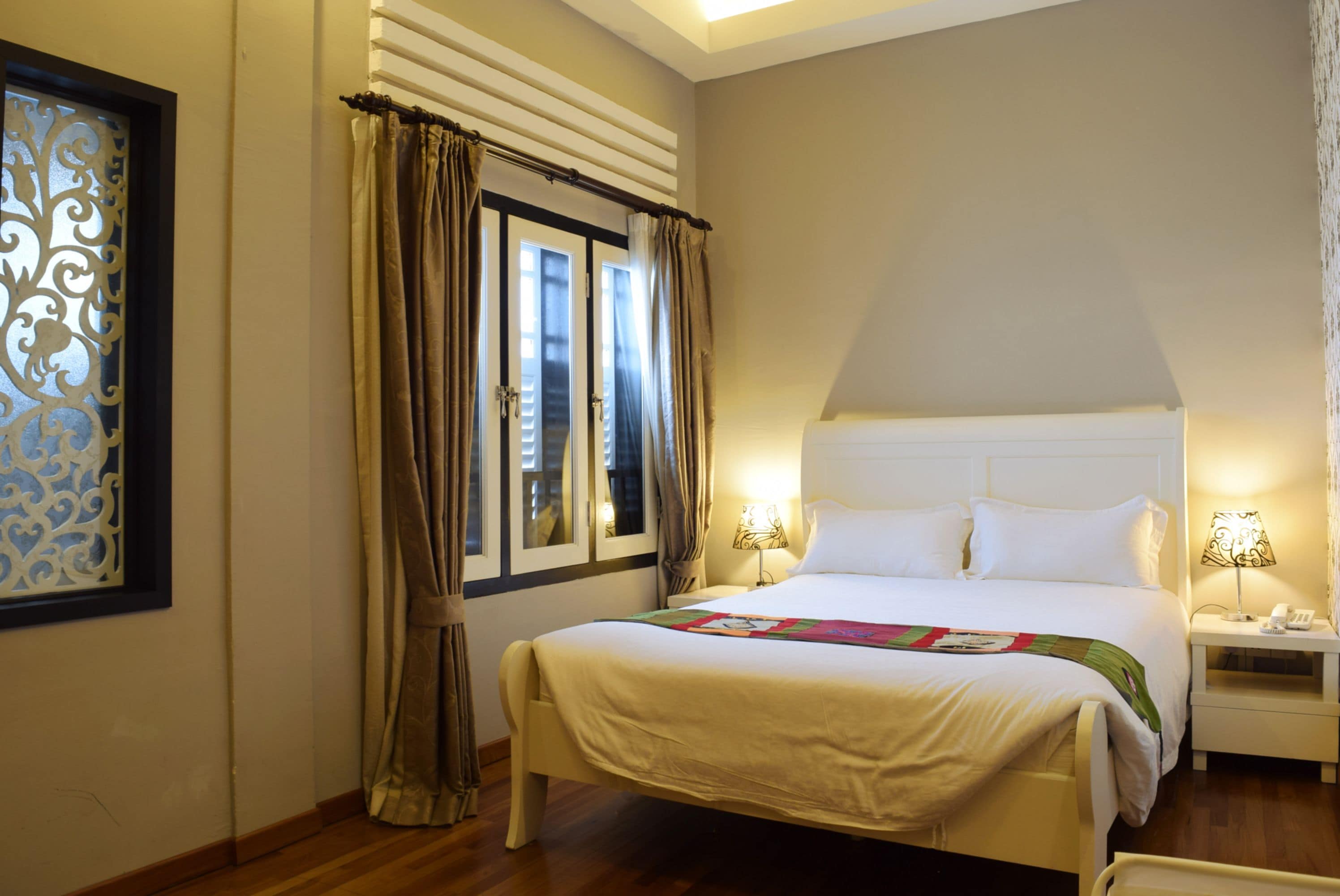 A hotel room with a large bed, two bedside tables with lamps, a window with curtains, and a decorative wall panel.
