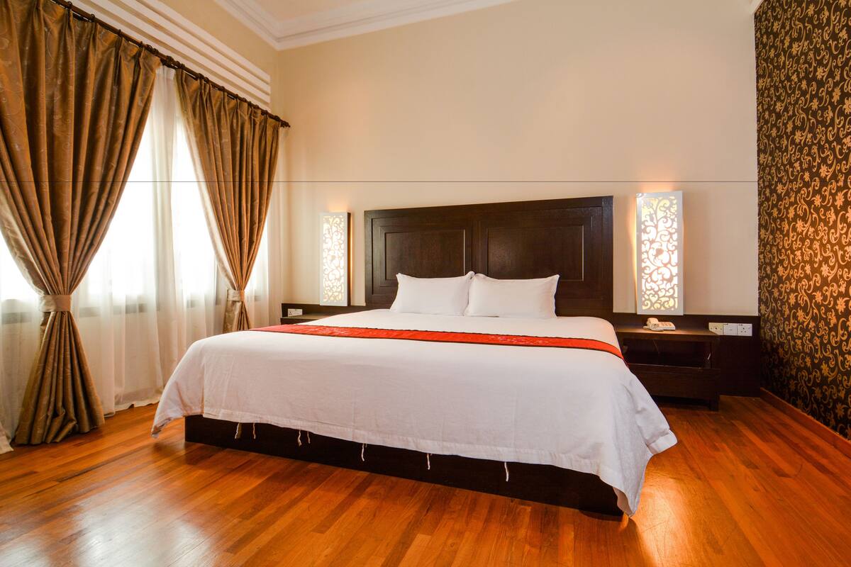 A large bed with a wooden headboard, white bedding, and a red accent.