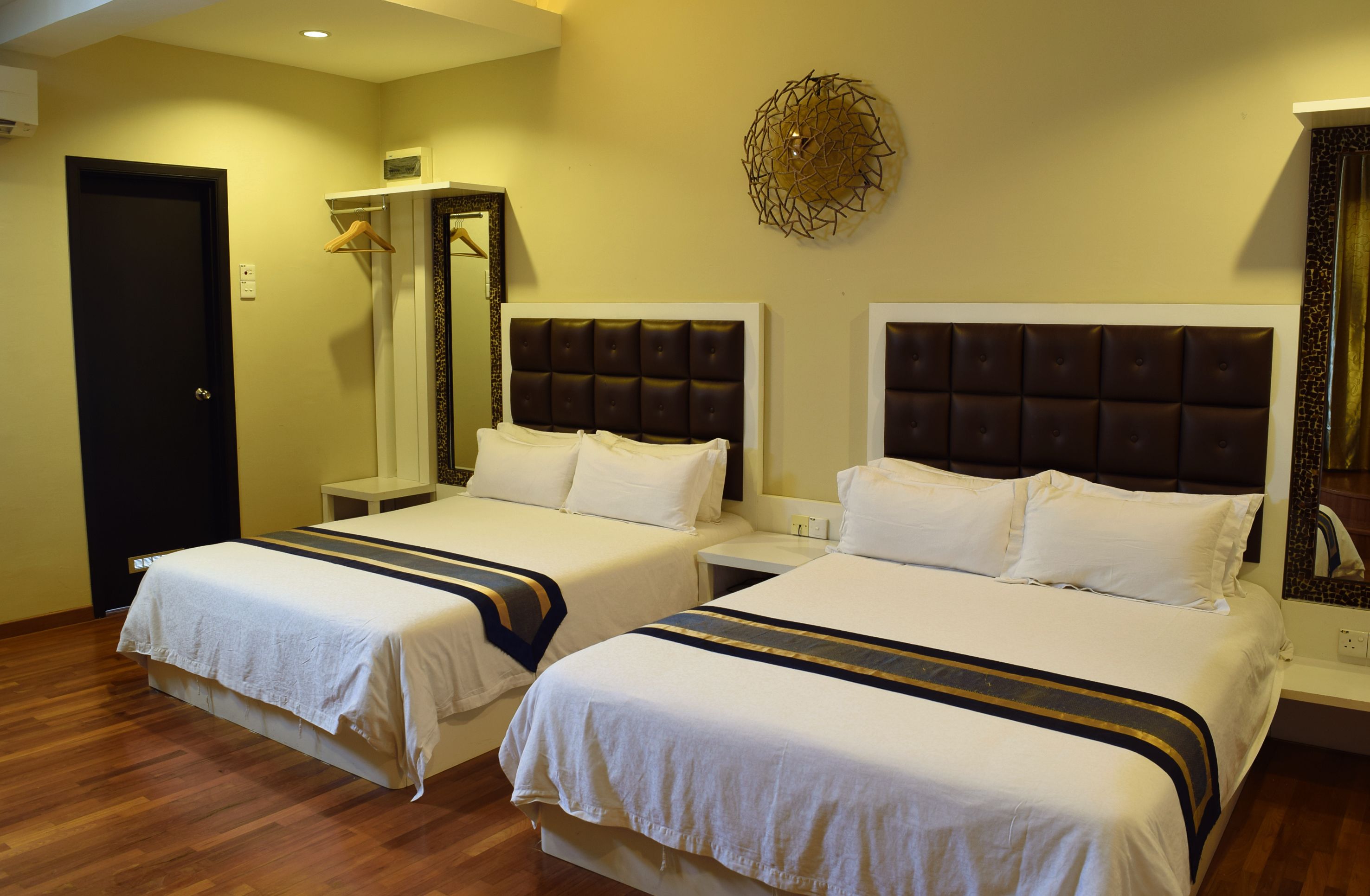 A hotel room with two beds, a wardrobe, a mirror, and a decorative wall piece.