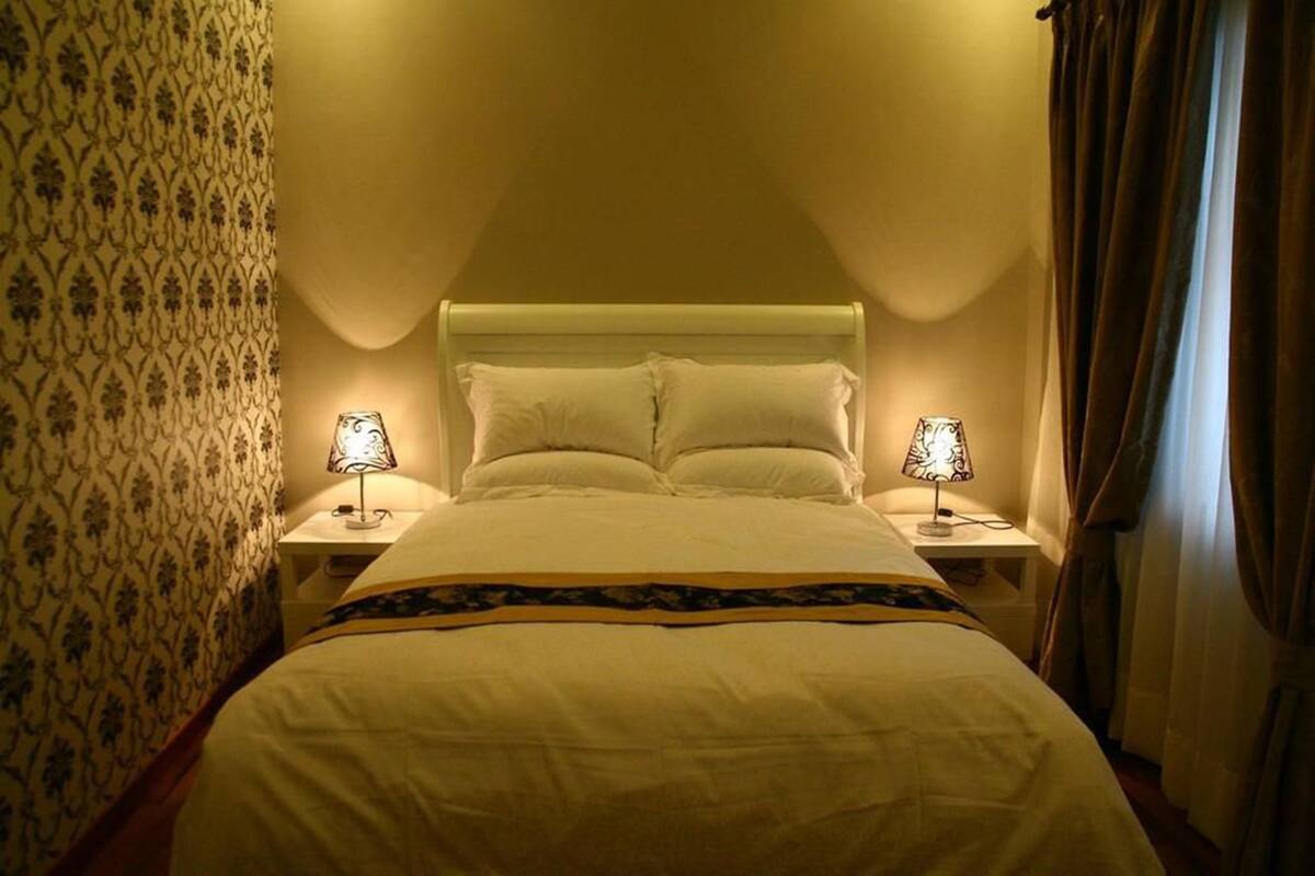 A hotel room with a bed, two bedside lamps, patterned wallpaper, and a curtain.