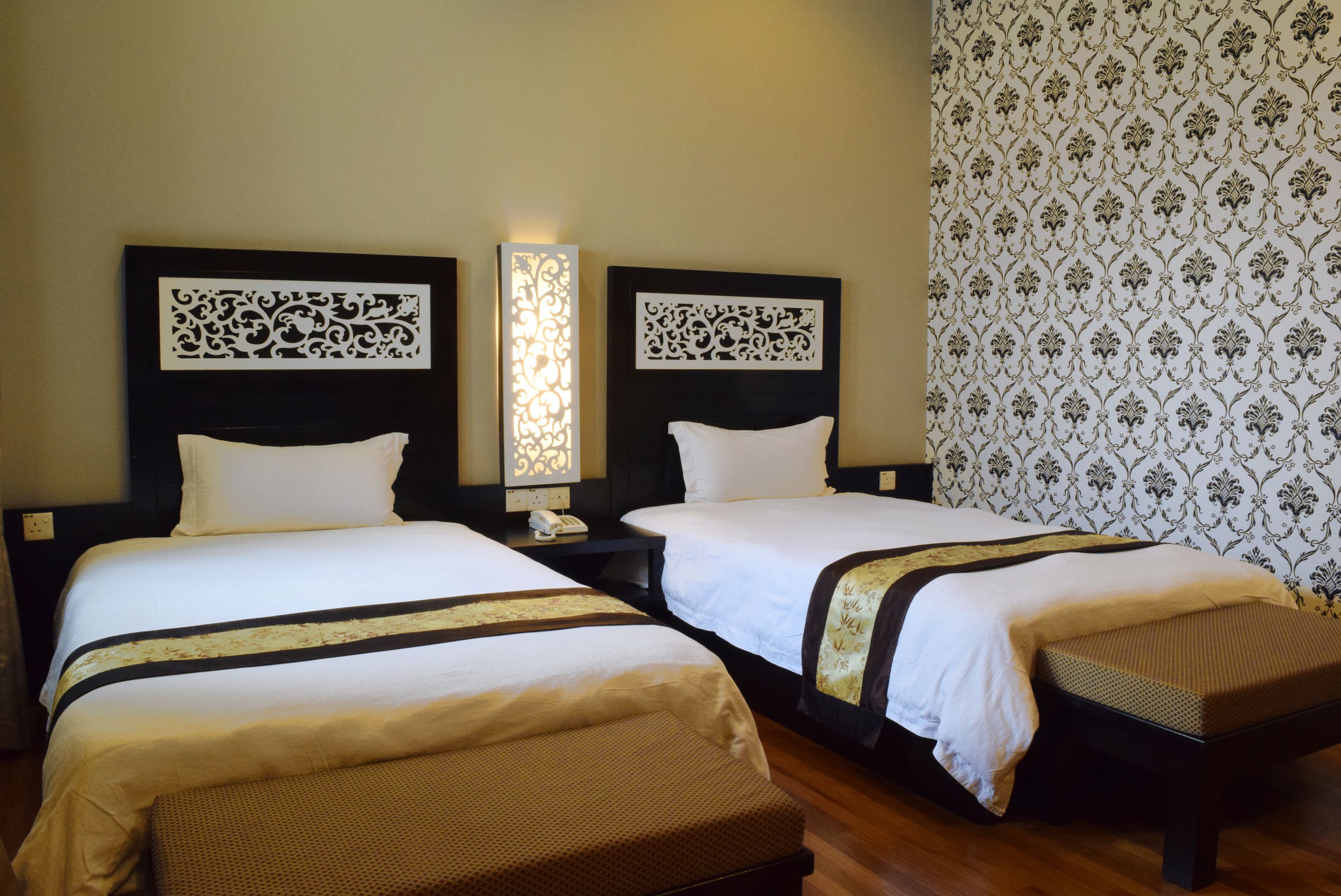 A hotel room with two beds, a nightstand with a phone, and a decorative wall panel.