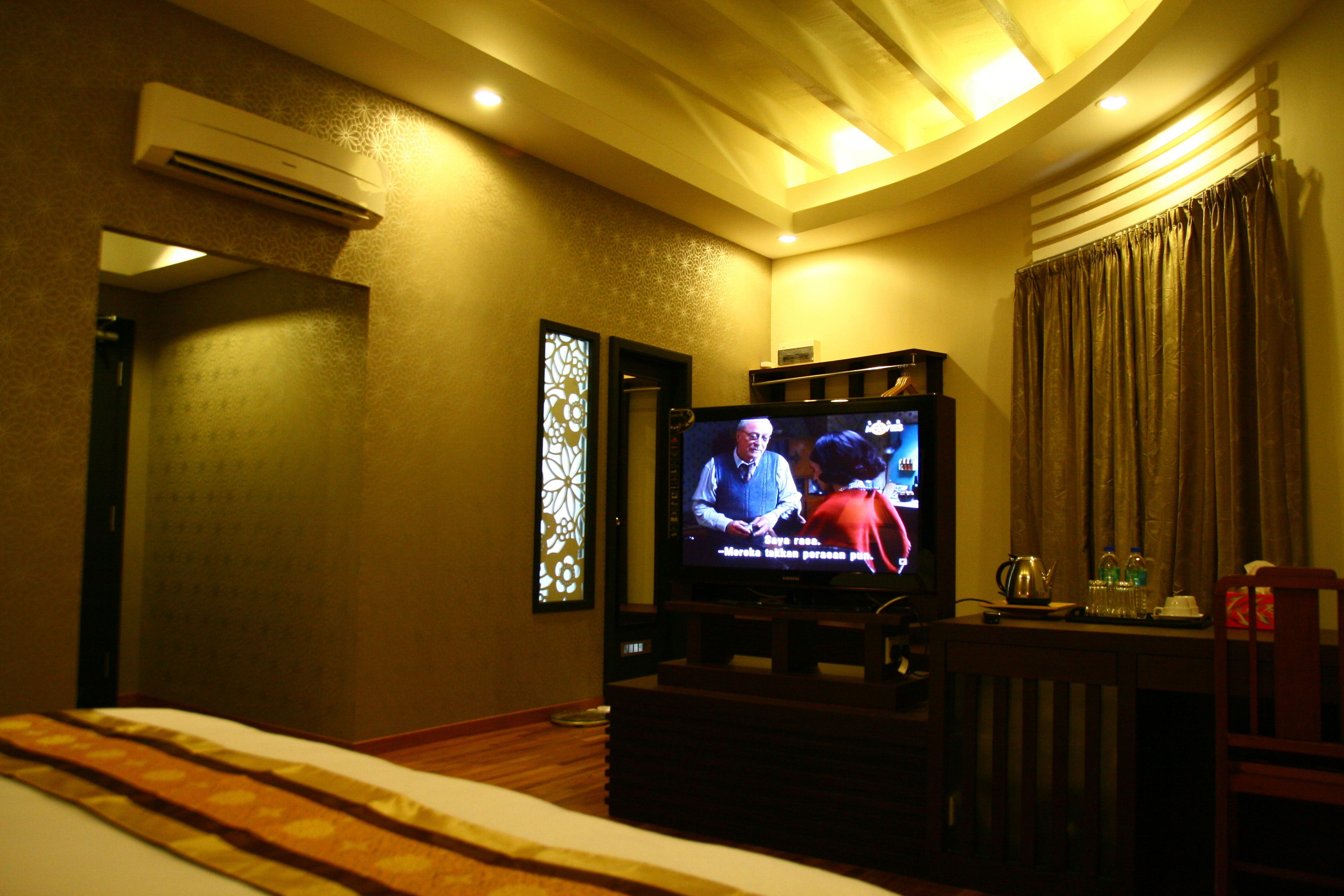 A hotel room with a television, a bed, a small table with a kettle, and curtains.