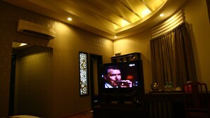 Une chambre d’hôtel faiblement éclairée, équipée d’une télévision, d’un ventilateur de plafond et d’une fenêtre avec des rideaux.