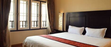A hotel room with a large bed, a dark headboard, and a window with curtains.