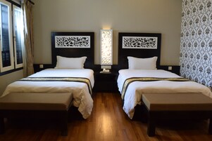 A hotel room with two beds, wooden flooring, and decorative wall panels.