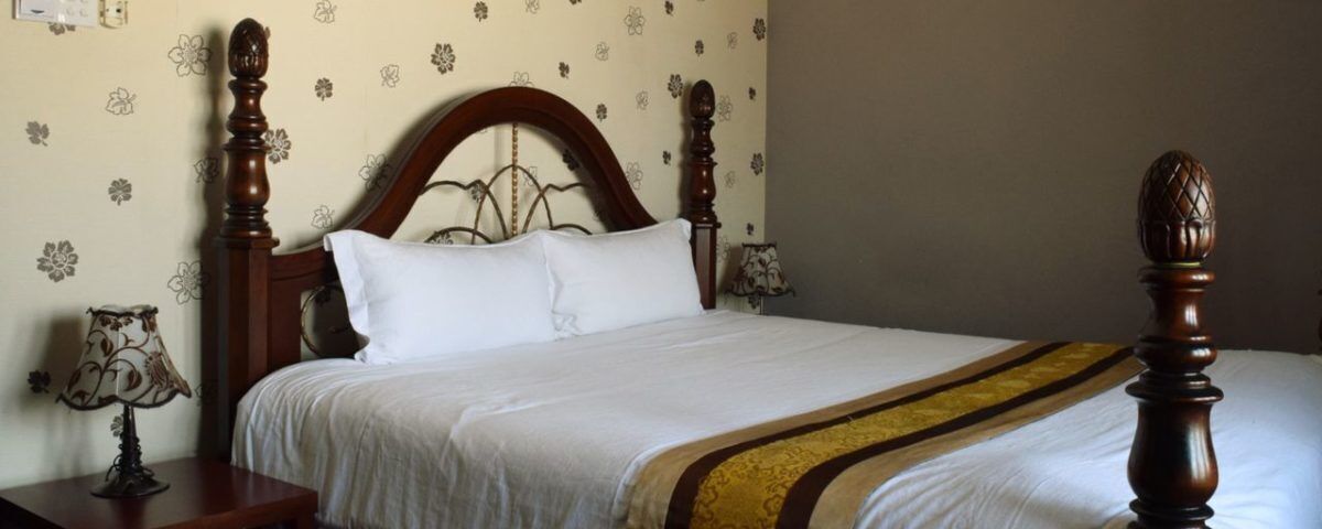 A neatly made bed with a wooden headboard, white bedding, and a decorative throw blanket.