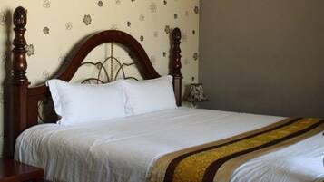 Cama bem arrumada com cabeceira de madeira, roupa de cama branca e manta decorativa.