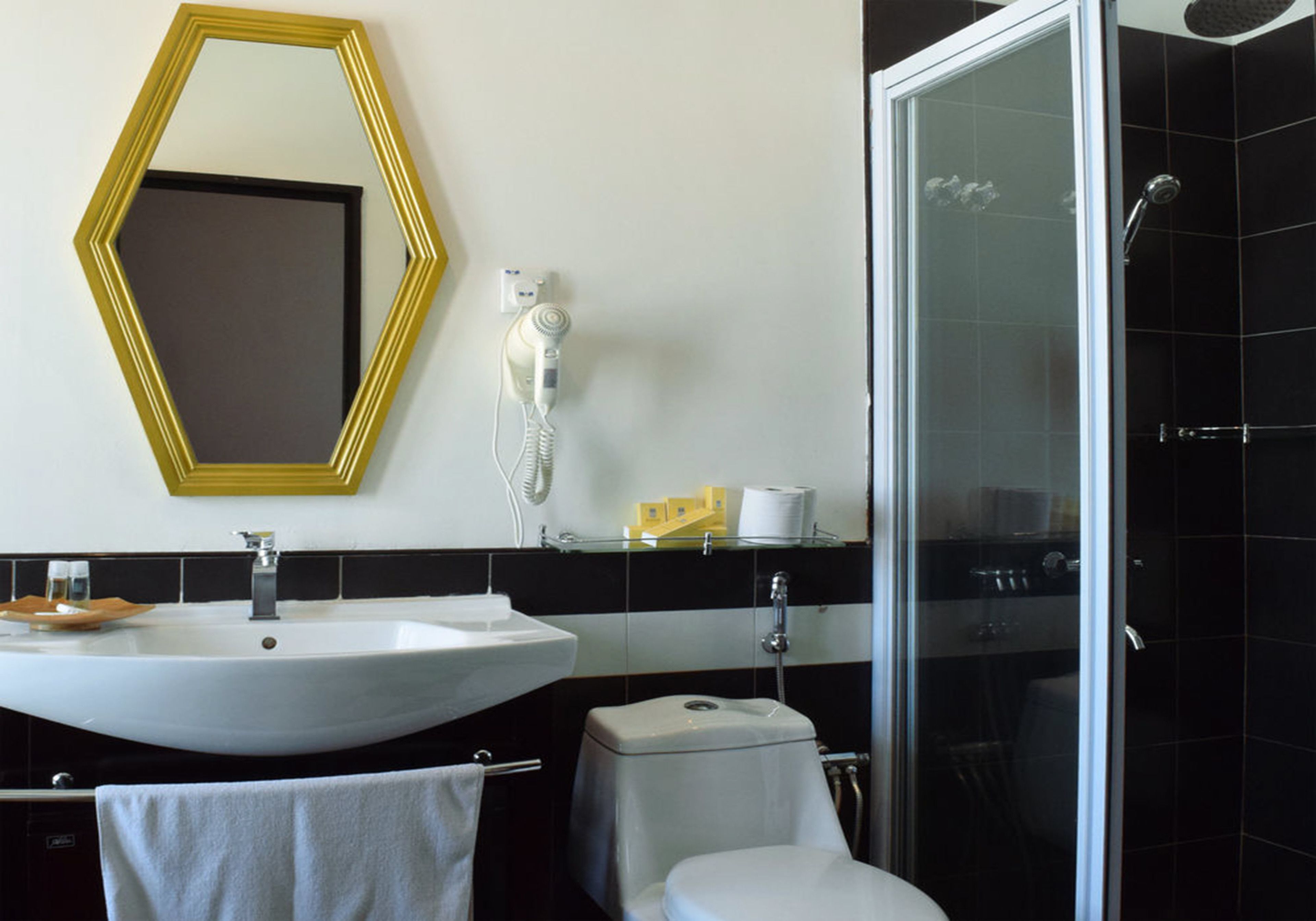 Une salle de bain moderne avec un lavabo blanc, des toilettes, une douche en verre et un miroir avec un cadre doré.