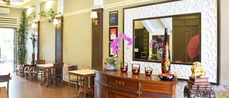 A hotel lobby with wooden furniture, a reception desk, and decorative elements like orchids and a golden lion statue.