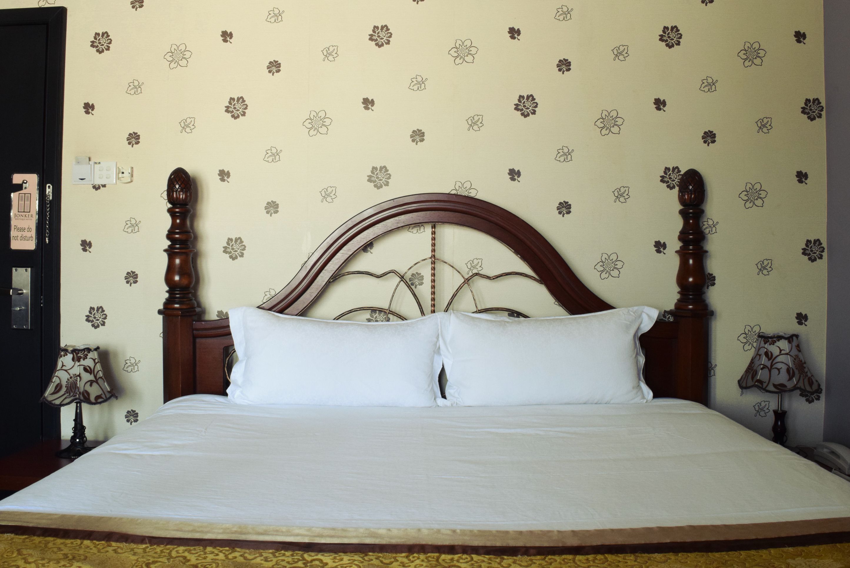 Ein Bett mit Holz-Kopfteil, weißer Bettwäsche und blumenmuster-tapizierten Wänden.