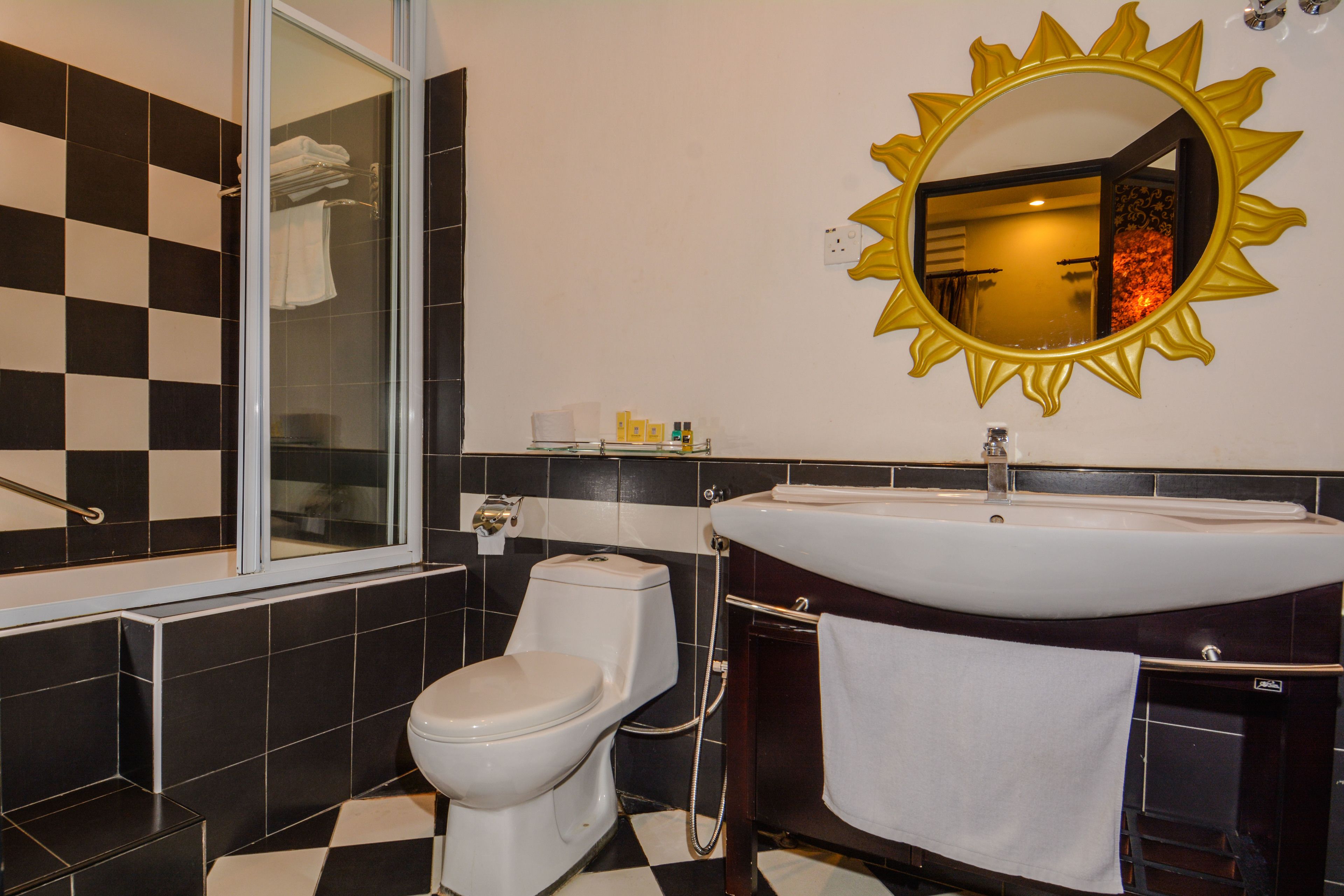 A bathroom with a checkered floor, a white toilet, a bathtub, and a sink with a golden mirror.