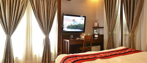 A hotel room with a bed, a desk with a television, and curtains.