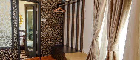 A room with a curved sofa, a glass-top table, a wooden floor, patterned wallpaper, and a staircase with a wooden railing.