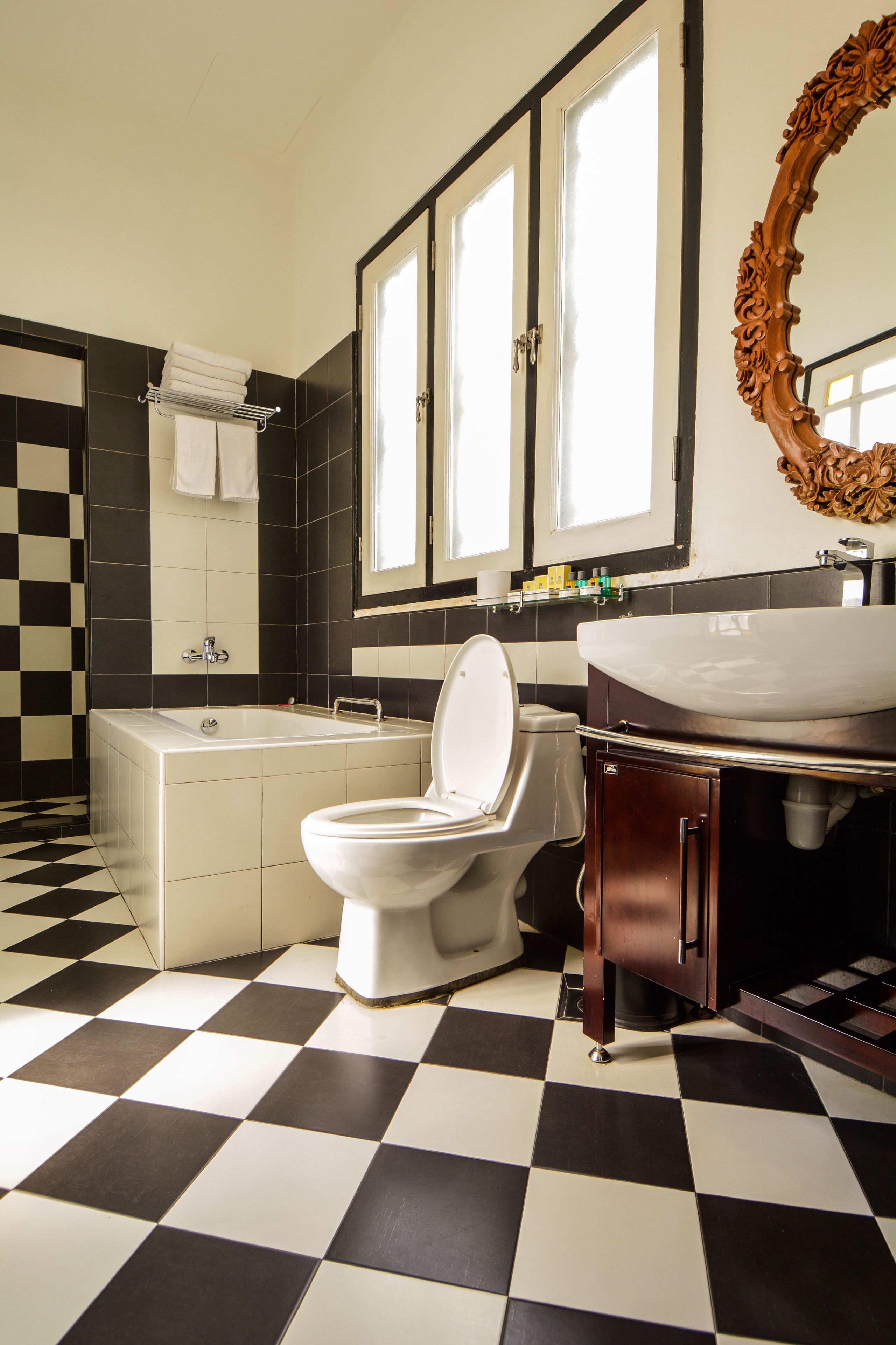 Une salle de bain avec un carrelage à motifs géométriques, une baignoire, des toilettes, un lavabo et un miroir orné d’un cadre travaillé.
