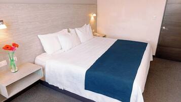 Habitación de hotel con cama, mesita de noche, un jarrón con flores y una lámpara de pared.