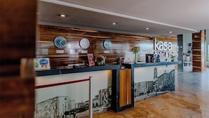 Vastaanottotiski, jossa on kelloja, kyltti, jossa lukee ”Kasa Hotel & Suites”, ja puinen seinäpaneeli.