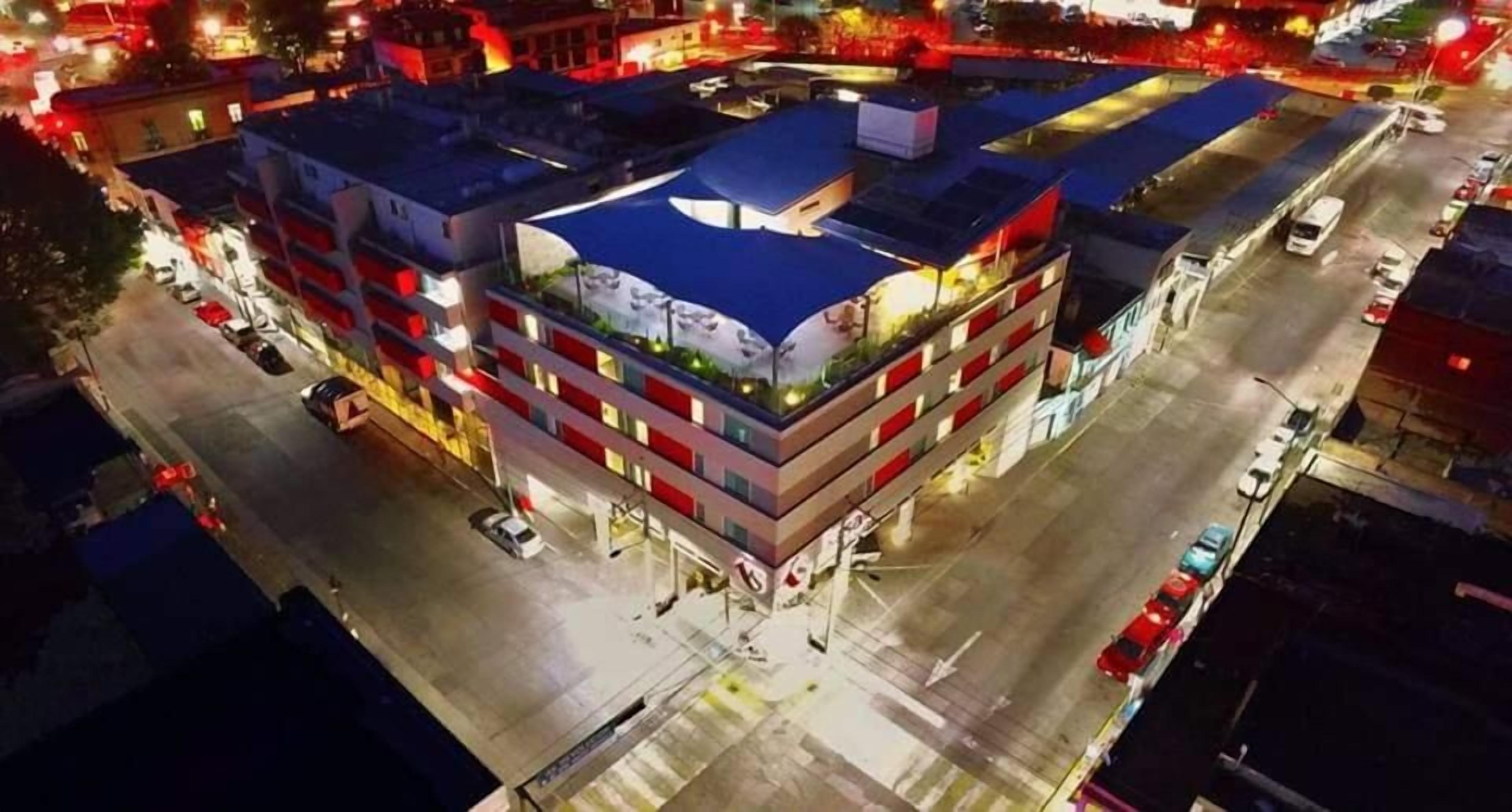 A multi-story hotel with a rooftop terrace, parking area, and adjacent buildings.